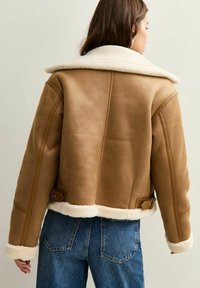 Giacca in shearling marrone con ampio colletto bianco, design corto e dettagli con fibbia sui lati. Finitura in pelle testurizzata.