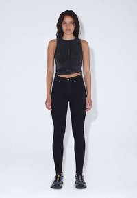 Černý krátký top a přiléhavé černé džíny v kombinaci s černou sportovní obuví s barevnými akcenty. Hladká textura, elegantní design.