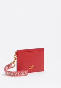Portafoglio rosso con texture e logo dorato "BIMBA Y LOLA", dotato di una tracolla staccabile con stampa del logo in rosa e bianco. Forma compatta e rettangolare.