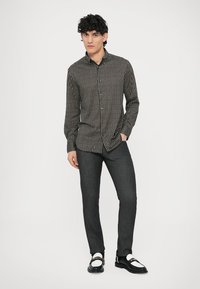 Fekete, gombos ing geometrikus fehér mintával, hosszú ujjú, sötét farmerrel és fekete-fehér cipővel párosítva.