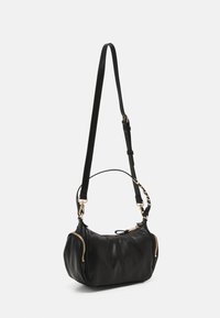 Bolso de mano de cuero negro con forma redondeada, que cuenta con cremalleras doradas a cada lado y una correa ajustable para mayor versatilidad.