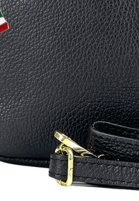Schwarze Lederhandtasche mit strukturierten Oberflächen, goldenen Beschlägen und einem Akzent im italienischen Flaggenmotiv. Verfügt über einen Tragegurt und eine schlanke Form.