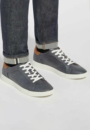 Grijze leren sneakers met witte veters, afgeronde neus en tan accenten op de hiel. Geribbelde afwerking en contrasterende rubberen zool.