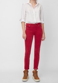 Rode corduroy broek met een slim fit, voorzien van een knoopsluiting en opgerolde pijpen, gecombineerd met een wit shirt en bruine veterschoenen.
