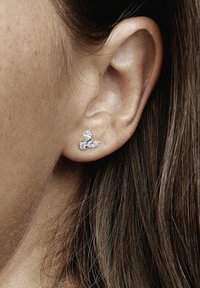 Strieborné náušnice so dvoma kamienkami v tvare marquise a jedným okrúhlym, zasadené v minimalistickom dizajne, nosené na uchu.