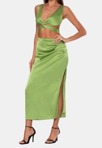 Groene satijnen deux-piece set met een gedraaide crop top en een rok met hoge split. De stof heeft een gladde textuur en een glanzende afwerking.