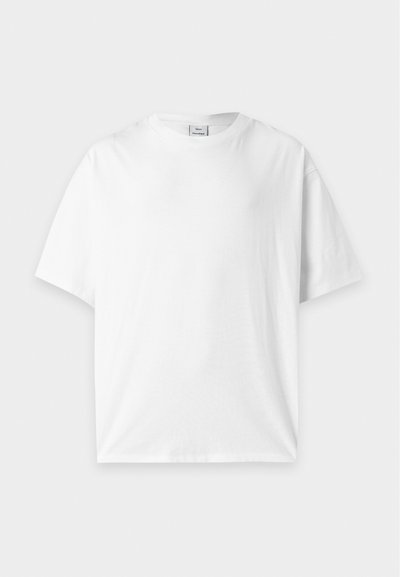 Απλό λευκό κοντομάνικο T-shirt με στρογγυλή λαιμόκοψη, τοποθετημένο επίπεδα σε ανοιχτό γκρι φόντο.