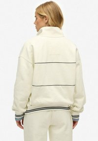 Cream-colored sweatshirt with a high collar, drop shoulders, and black horizontal stripes on the back. Soft fabric, relaxed fit.