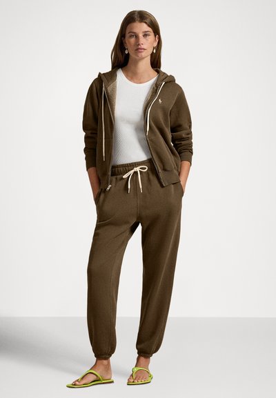 Brun bomulls hettejakke med glidelås foran, kombinert med matchende joggebukser med elastisk midje og snor, båret med grønne flip-flops.