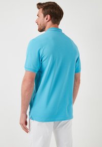 Polo majica v svetlo modri barvi, kratki rokavi, ovratnik, izdelana iz gladkega materiala. Ima stranske razpoke na robu in reden kroj.