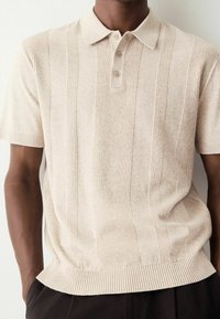 Polo en tricot beige avec texture côtelée verticale, patte de boutonnage à trois boutons et manches courtes, présentant un ourlet ajusté et un matériau doux.