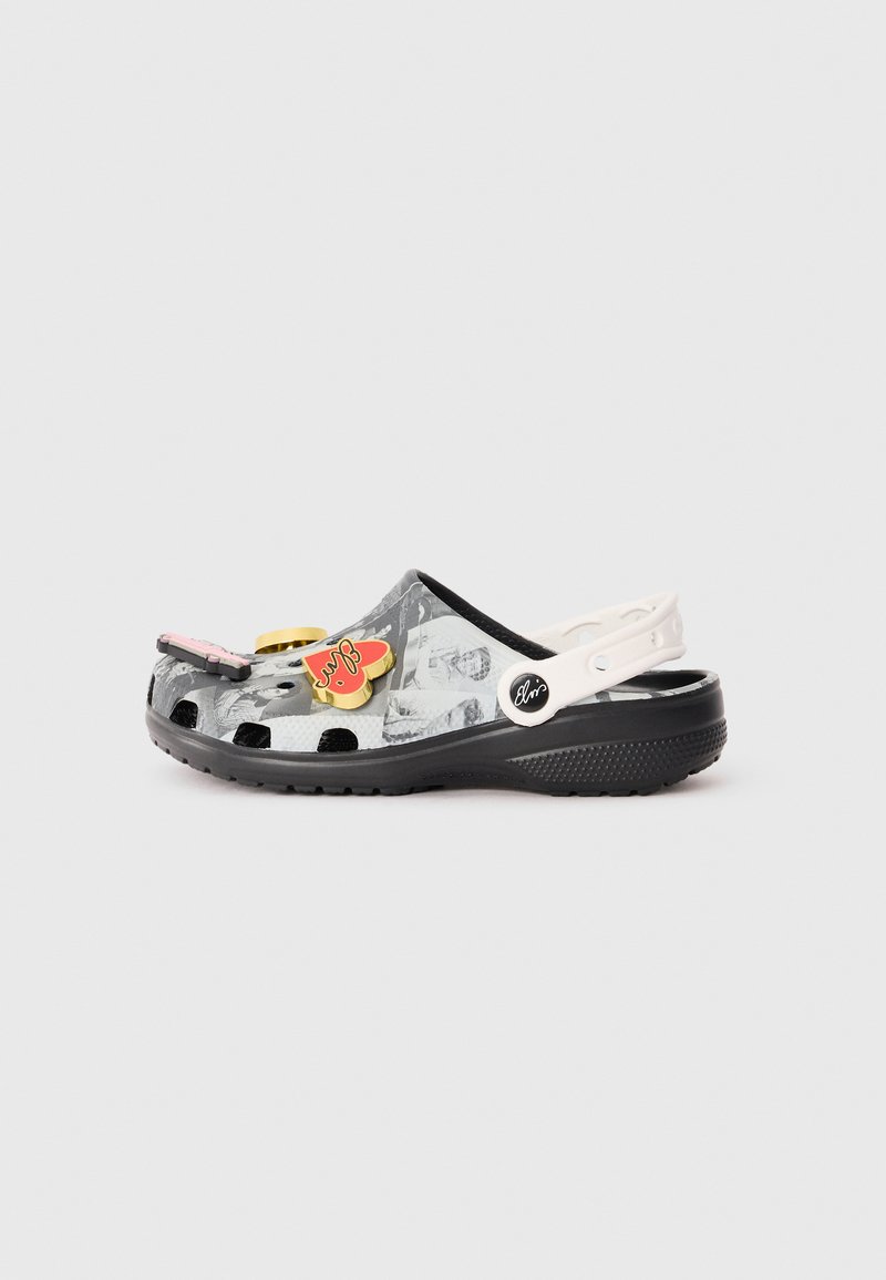 Svarte og hvite crocs med dekorative charms, med en teksturert overdel, rund tå og bred stropp. Lett design med ventilasjonshull.