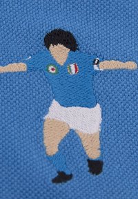 Borduurwerk van een voetballer in een blauw shirt met witte shorts. Bevat patches van de Italiaanse vlag en gedetailleerde gezichts- en ledemaataccenten.