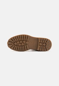 Suela de bota de goma marrón con un patrón texturizado y robusto para tracción. Presenta dibujos profundos y una impresión del logotipo circular. Diseño duradero y resistente.