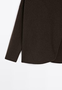 Dunkelbrauner Langarmpullover mit abgerundetem Saumdetail, hergestellt aus einem weichen, strukturierten Stoff vor einem weißen Hintergrund.
