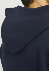 Navy Kapuzenpullover aus weichem Baumwollmix, mit lockerer Passform und strukturiertem Hoodie. Nähte sind am Ausschnitt sichtbar.