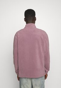 Fleece-pullover i ljus mauve med höga krage, avslappnad passform och långa ärmar. Mjuk textur och slät finish. Avslappnad design.