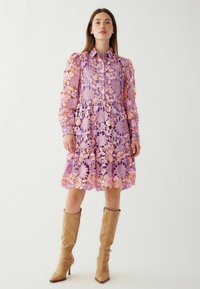 Violetinė ir rožinė gėlių nėrinių suknelė su mygtukų užsegimu, raukšlėtu apdailu, ilgomis rankovėmis ir derančiais aukštais, smėlio spalvos kulniukais.