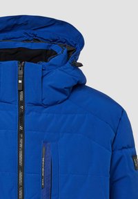 Niebieska ocieplana kurtka z wysokim kołnierzem, zamkiem błyskawicznym z przodu i kapturem. Posiada boczną kieszeń i pikowaną fakturę zapewniającą ciepło.