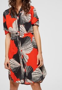 Abito rosso con maniche corte, caratterizzato da un motivo a foglie in bianco e nero, cintura in vita, vestibilità comoda e lunghezza fino al ginocchio.