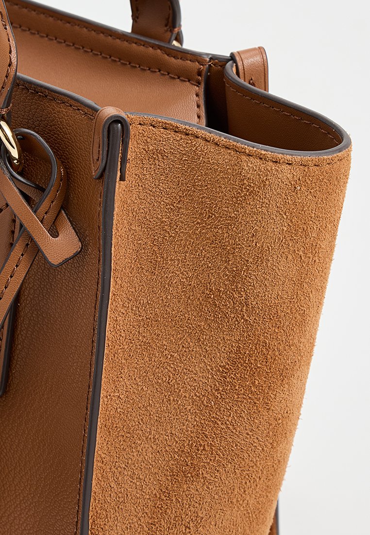 Bolso de piel de gamuza marrón con acentos de cuero suave. Presenta una textura suave, líneas limpias y detalles de costura en contraste.