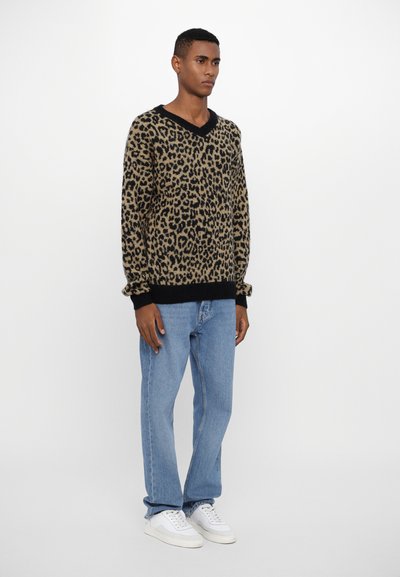 Leopard print sweater in beige and black, featuring a V-neckline and ribbed cuffs, paired with light blue jeans and white sneakers.