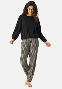 Zwarte langslavige top met een elastische tailleband, gecombineerd met gestreepte, losse broek met verticale zwarte en crèmekleurige lijnen.