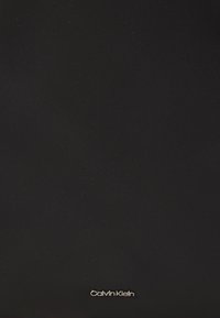 Bolso negro de Calvin Klein hecho de tejido texturizado, con un acento de logo plateado en la parte inferior. Diseño simple y minimalista sin patrones adicionales.