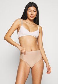 Light pink ribbed bralette with thin straps paired with high-waisted nude underwear, showcasing smooth texture and seamless design.