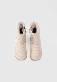 Stivali da neve imbottiti in beige chiaro, caratterizzati da un design trapuntato, suola in gomma grigia e cerniere laterali per una facile vestibilità.