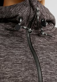 Szara bluza rozpinana z teksturowanej tkaniny, z wysokim kołnierzem, czarnym zamkiem błyskawicznym oraz sznureczkami z czarno-białymi akcentami.