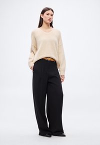 Béžový oversize pletený sveter s výstrihom do V a voľným strihom, skombinovaný s čiernymi širokými nohavicami s vysokým pásom a hnedým opaskom.