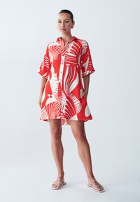 Abito rosso con motivi astratti bianchi, maniche corte, chiusura a bottoni sul davanti e vestibilità comoda, realizzato in tessuto leggero. Indossate sandali piatti.