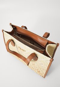 Tote bag with woven straw body, tan leather handles and accents. The interior features an organizational pocket and zipper closure.