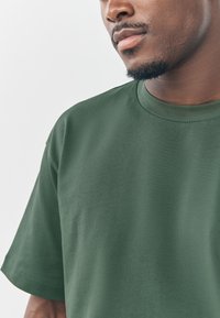 Grünes T-Shirt mit kurzen Ärmeln aus strukturiertem Stoff. Verfügt über einen Rundhalsausschnitt und eine lockere Passform.