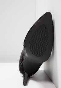 Černá dámská lodička s vysokým podpatkem, špičatou špičkou, strukturovaným svrškem a vroubkovanou gumovou podrážkou, nakloněná na světlém pozadí.