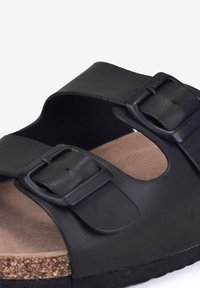 Schwarze Sandale mit zwei verstellbaren Schnallenriemen, strukturiertem, synthetischem Obermaterial und Korkfußbett. Die Sohle hat ein flaches, langlebiges Design.