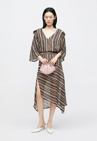 Stripete lang kjole i gjennomsiktig stoff med V-hals, flagrende ermer og en sidesplitt; kombinert med en rosa håndveske og hvite hæler.