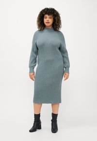 Stickad klänning i dämpad teal, ribbad textur, hög hals, långa ärmar. Bärs med svarta ankelboots. Längd till mitt på vadbenet.