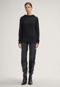 Zwarte gebreide hoodie met een textuurpatroon, voorzien van een trekkoord, lange mouwen en gecombineerd met donkergrijze aangesloten broeken en kniehoge zwarte laarzen.