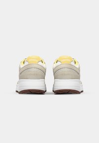 Sneakers featuring a beige suede upper with mesh accents, yellow heel tab, and white midsole. Brown rubber outsole with textured tread.