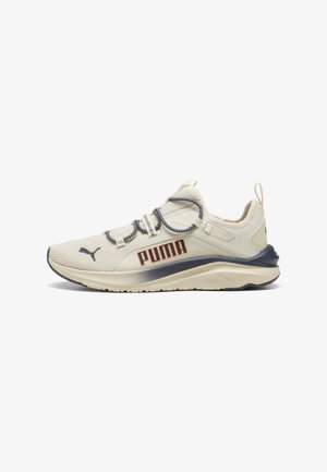 Scarpa sportiva beige con parte superiore in mesh testurizzato, logo arancione a contrasto e dettagli grigi. Presenta lacci elastici e un tallone modellato.