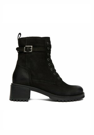 Schwarzer Lederknöchelstiefel mit Schnürung vorne, seitlichem Riemen mit Schnalle, klobigem Absatz und Zuglasche vor weißem Hintergrund.