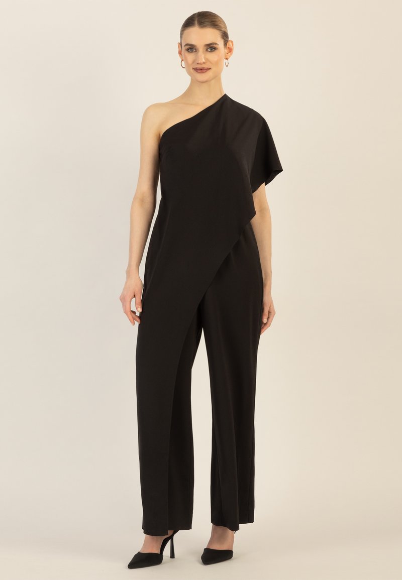 Zwarte één-schouder jumpsuit met gedrapeerde textuur en asymmetrisch ontwerp, voorzien van wijde pijpen en een slim fit, gecombineerd met puntige zwarte hakschoenen.