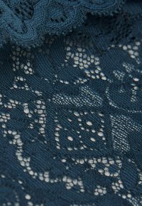 Navy blauw kantstof met ingewikkelde patronen, openingen en een gestructureerde afwerking. De randen hebben een geschulpte vorm.