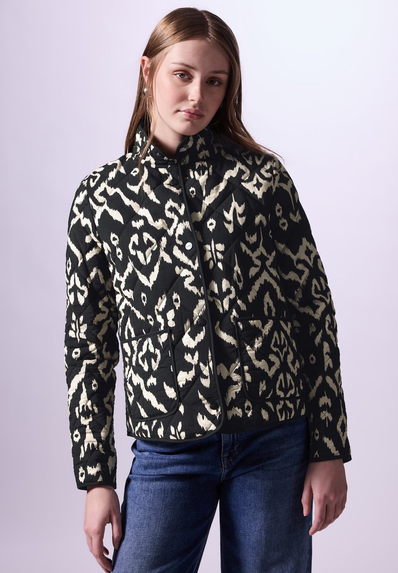 Schwarz-weiße gesteppte Jacke mit abstraktem Muster, ausgestattet mit einem hohen Kragen, zwei Fronttaschen und Knopfverschluss.