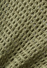 Gros plan d’un tissu tricoté vert avec un motif diagonal en maille ouverte et des brins de fil texturés.