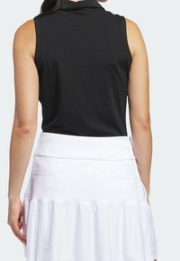 Polo noir sans manches avec une texture côtelée et un col montant, associé à une jupe-short blanche avec un ourlet à volants et des poches latérales.