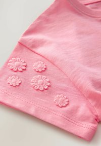 Roze katoenen t-shirt met zes geborduurde bloemenmotieven op de mouw, met een zachte textuur en een eenvoudige ronde halslijn.