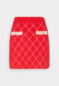 Gonna mini rossa lavorata a maglia con un motivo a rombi, accentuata da piccoli gioielli e due tasche rosa chiaro con bottoni argentati.